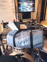 Load image into Gallery viewer, Symmetrical Drumming V3 - Duffel Bag (Grey) - Large kit bag sitting on drums holding drumsticks and sheet music - side view - Keen Eye Design
